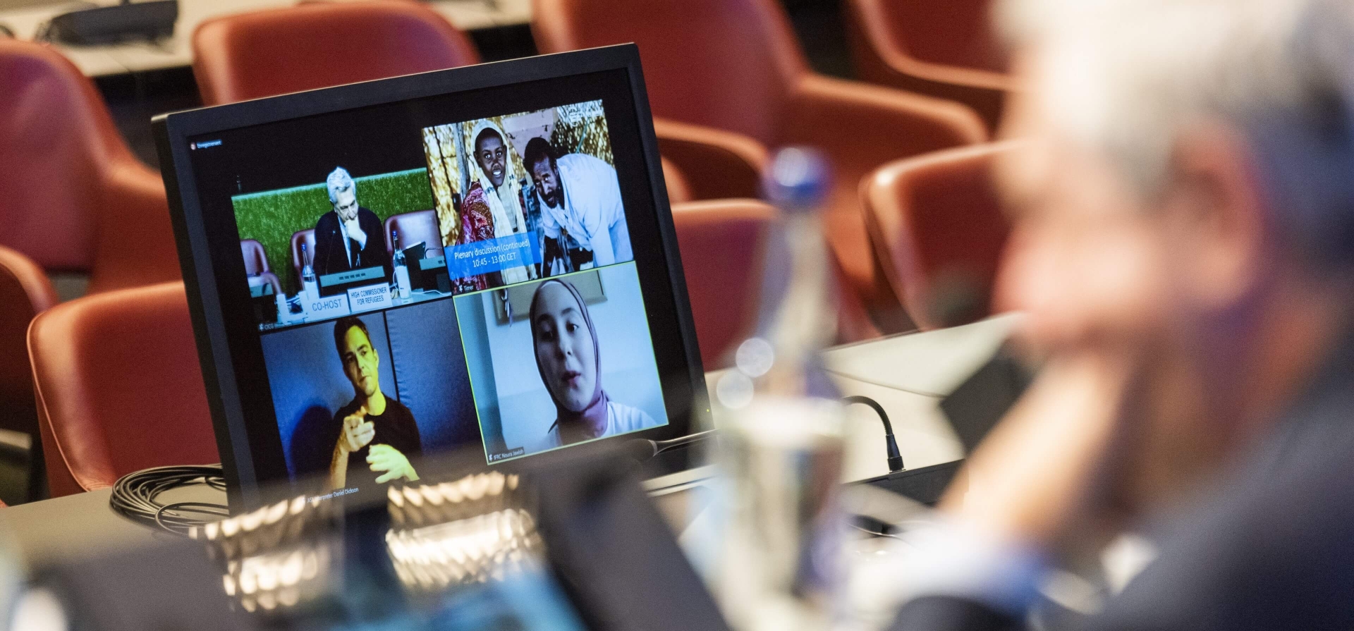 A view from over the shoulder of the High Commissioner, who is looking at screens of virtual participants