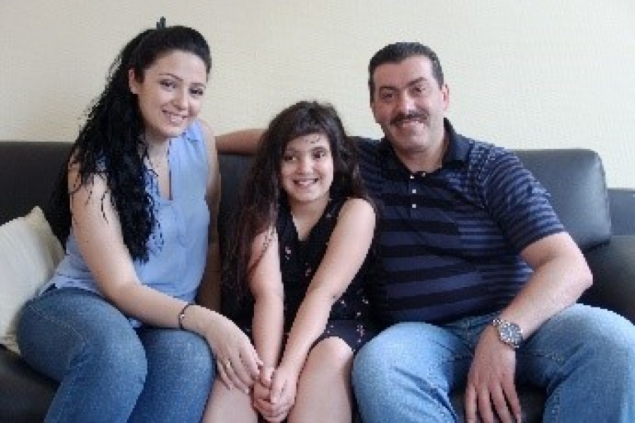 A woman, man and a child smiling at the camera sitting in a couch.