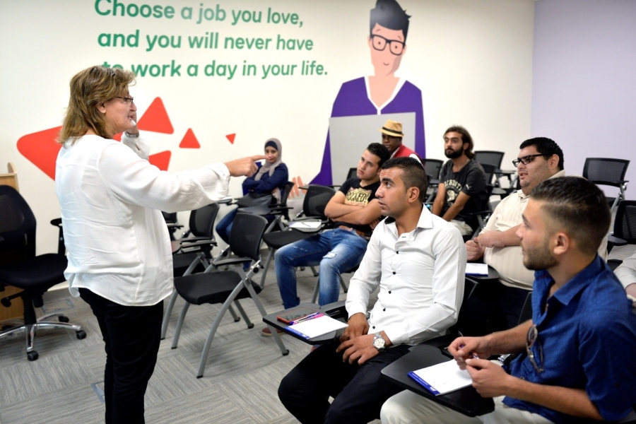 People seated listening to a woman talking in front of them.