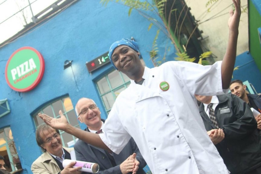 A chef standing with his hands up and smiling, while others clap.
