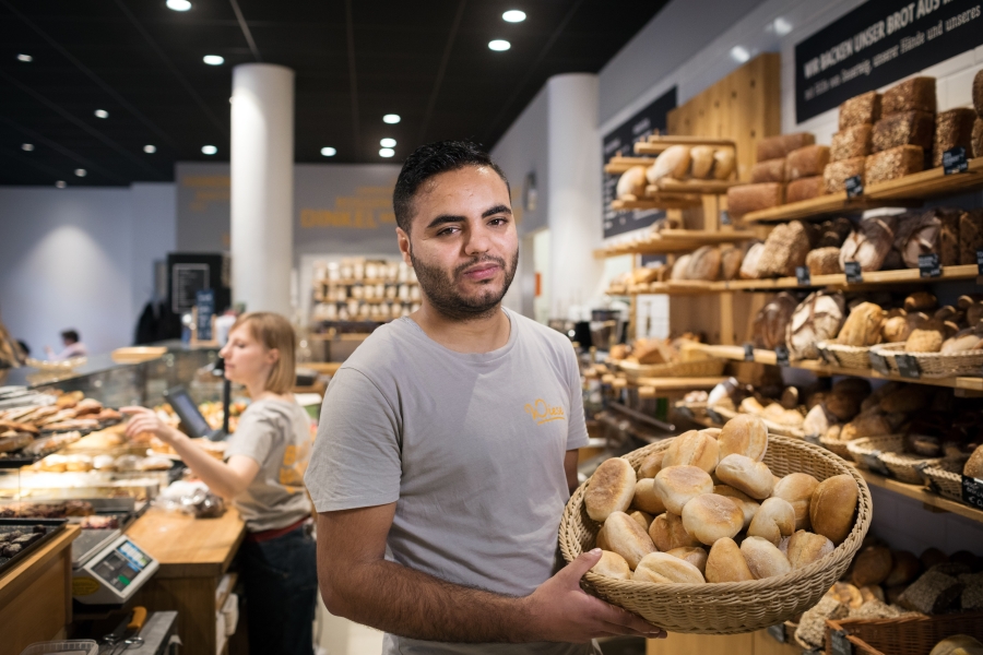 A baker stands with showing a basket of bread behind a shop counter