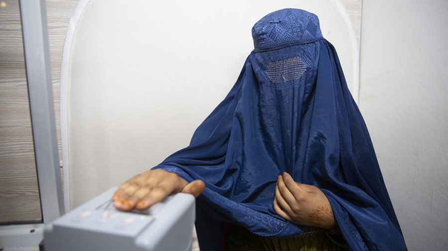 A woman wearing a burqa is having her fingerprints scanned
