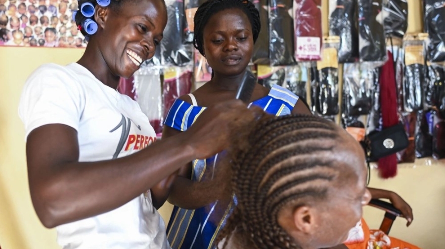 A woman braids the hair of another woman while a third woman watches on