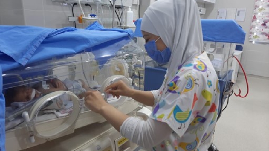 A woman wearing a mask is working in a neonatal intensive care unit.