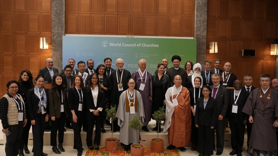 Religious representatives pose for a photo during the event ‘Religious Leaders Unite for Climate Peace in Solidarity with Refugees’, one of many discussions at the Global Refugee Forum 2023 - they are standing in a group facing the camera, with three potted trees in front of them.
