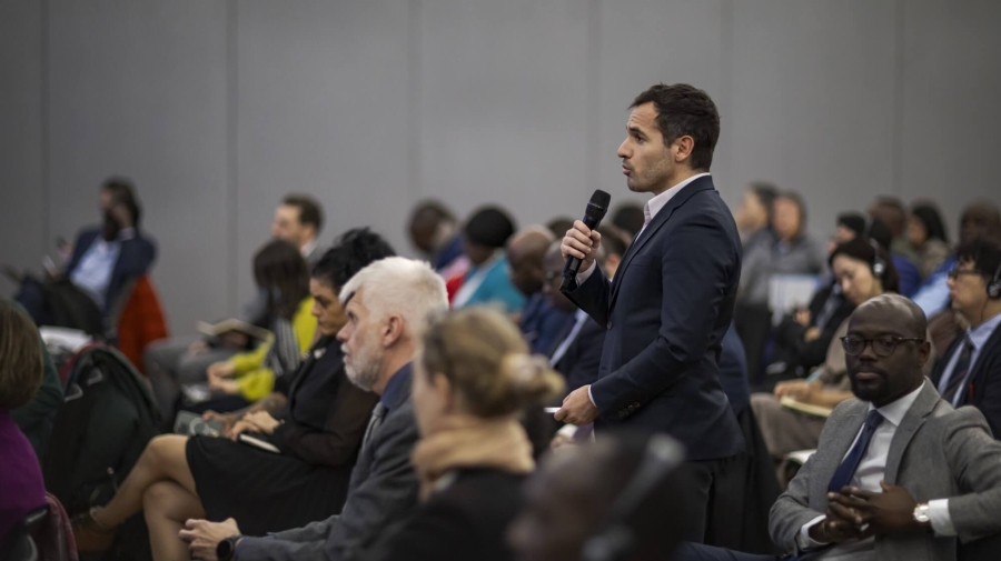 A man standing up in the audience of an event, speaking into a microphone