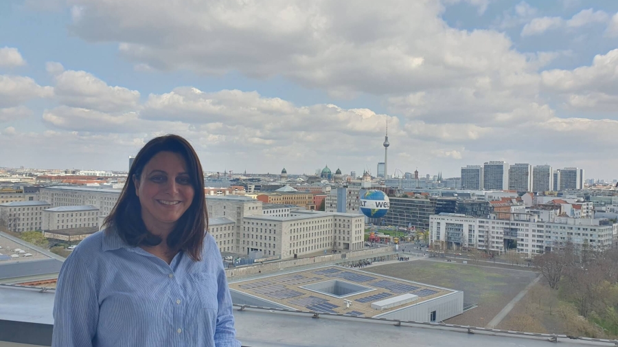 Taban standing on the balcony of German Federal Ministry for Economic Cooperation and Development, behind her is the Berlin skyline, with the TV Tower (Fernsehturm) and Berlin Cathedral (Berliner Dom) in the distance and the Welt hot air balloon in the foreground. The sky is blue with white/light grey clouds.