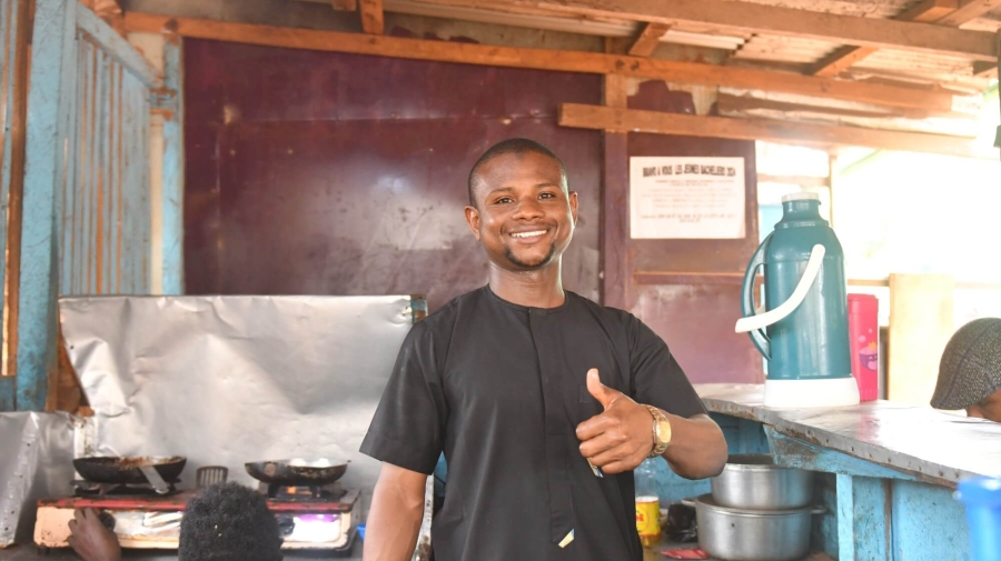 A man standing in a restaurant kitchen. He is smiling and giving a thumbs up to the camera