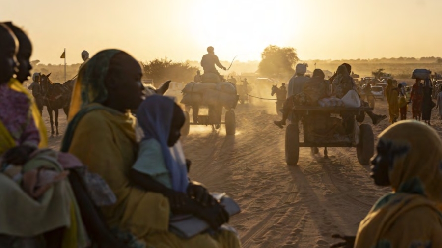 The sun lights up the dust behind groups of Sudanese refugees walking and on carts behind horses
