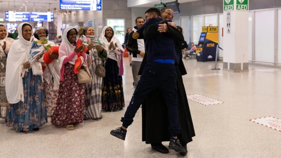 Father Solomon embraces tightly his youngest son, Yoftahie, who has just landed to Athens with his mother and siblings under the gaze of female members of the Eritrean Orthodox congregation in Greece, who joined Father Solomon welcoming his family at the International Airport of Athens